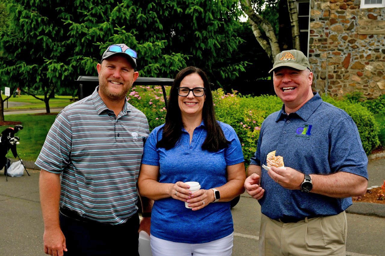 Three people smiling in front of landscaping