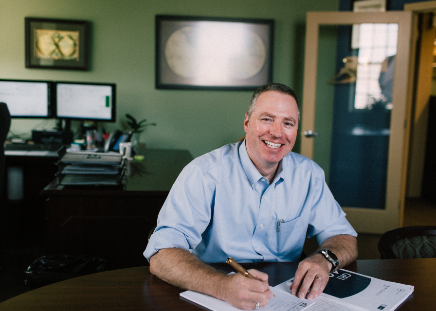 Headshot of Kent Schwendy sitting at a desk writing on a pad of paper