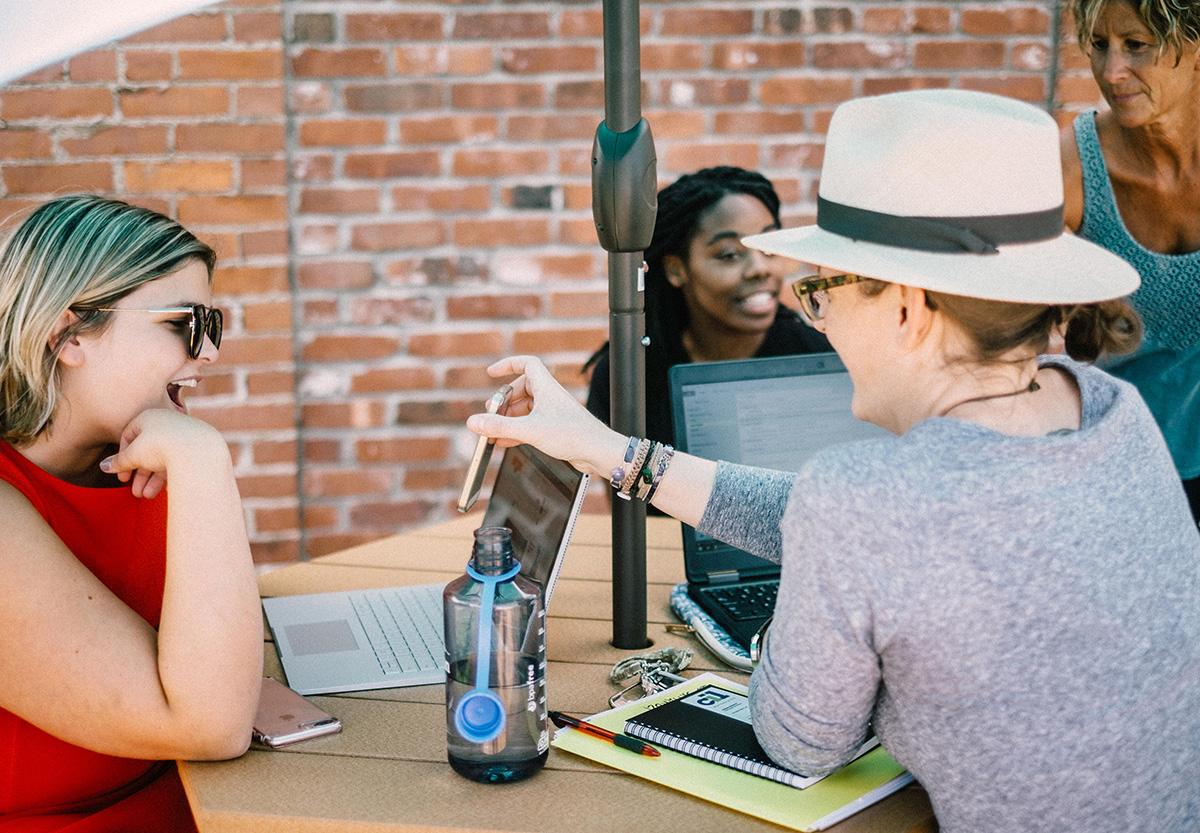 Image of women sitting at table working on their computers and talking