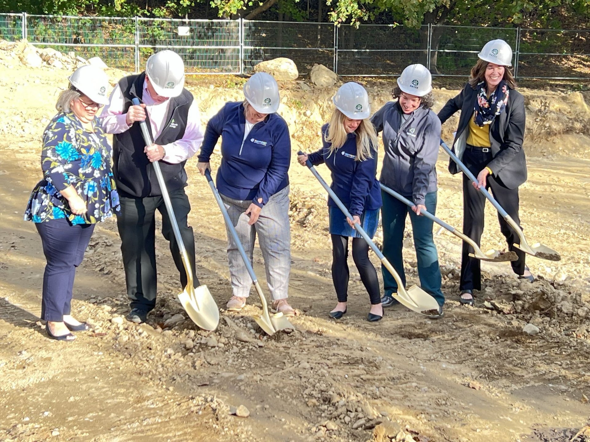 photo of six individuals with hard hats, all holding shovels which are actively being used to dig in dirt